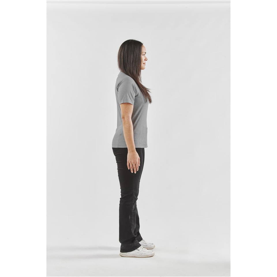 A woman stands sideways wearing a grey Women's Volante H2X-Dry Tee and black trousers, with a logo on the shirt.