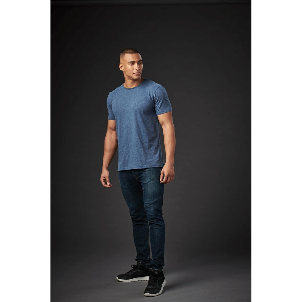 A crew neck t-shirt in blue, displayed on a male model against a dark background, paired with dark jeans and sneakers.