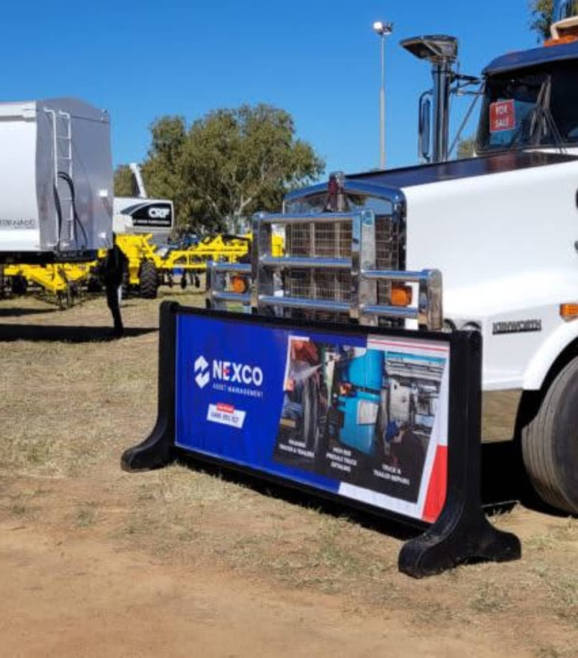 A signage barrier featuring a branded design, predominantly blue and red, displayed in an outdoor setting near equipment.