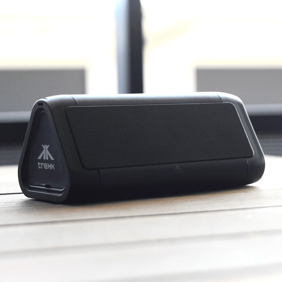 A black outdoor speaker with a triangular shape and a logo, resting on a wooden surface.