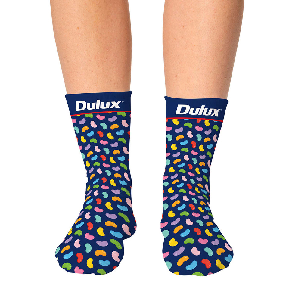 Colourful patterned socks with a navy background, featuring a playful design of multicoloured shapes and a logo on the cuff.