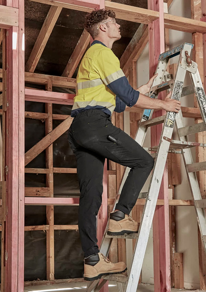 Men's lightweight outdoor cargo pants in black worn by a person on a ladder, set in a construction environment.