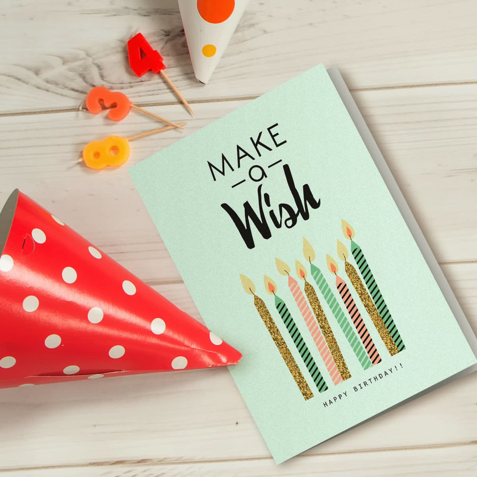 A light green gift card featuring birthday candles, surrounded by a red polka dot party hat and colourful candle numbers.