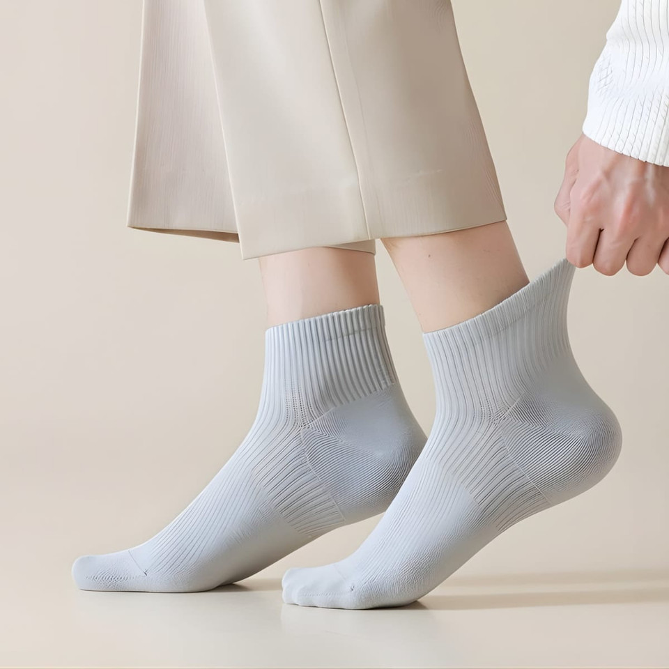 A pair of light grey socks is being pulled up, showcasing a ribbed design. The background is a neutral tone.