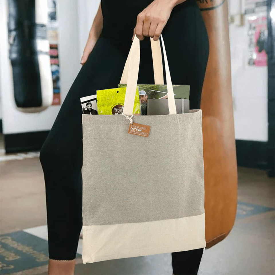 A beige and cream tote bag with a logo, held by a person, containing various items inside.