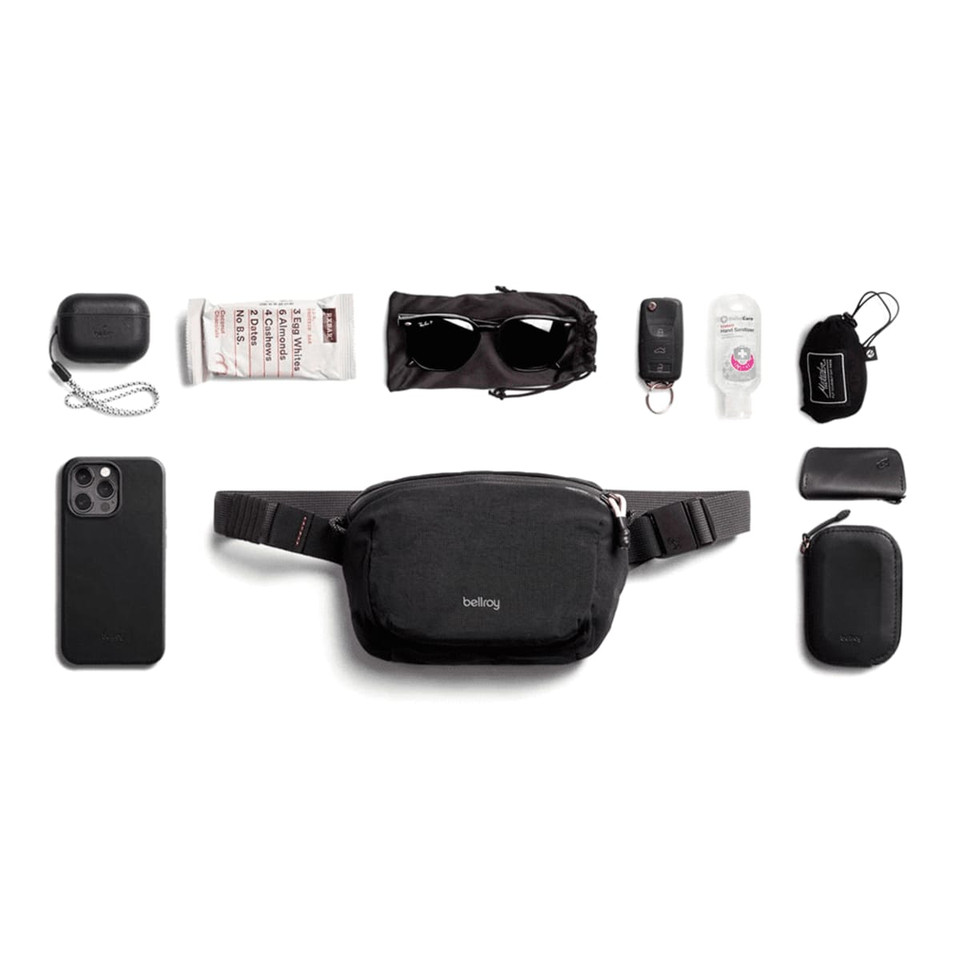 A black Bellroy Lite Belt Bag surrounded by various black items including a phone, sunglasses, and keychain.
