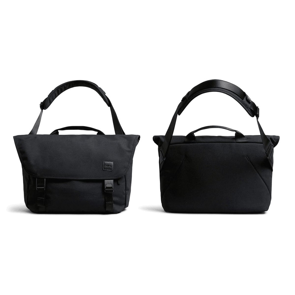 A black messenger bag with adjustable strap, featuring a flap closure and carry handles, along with a subtle logo.