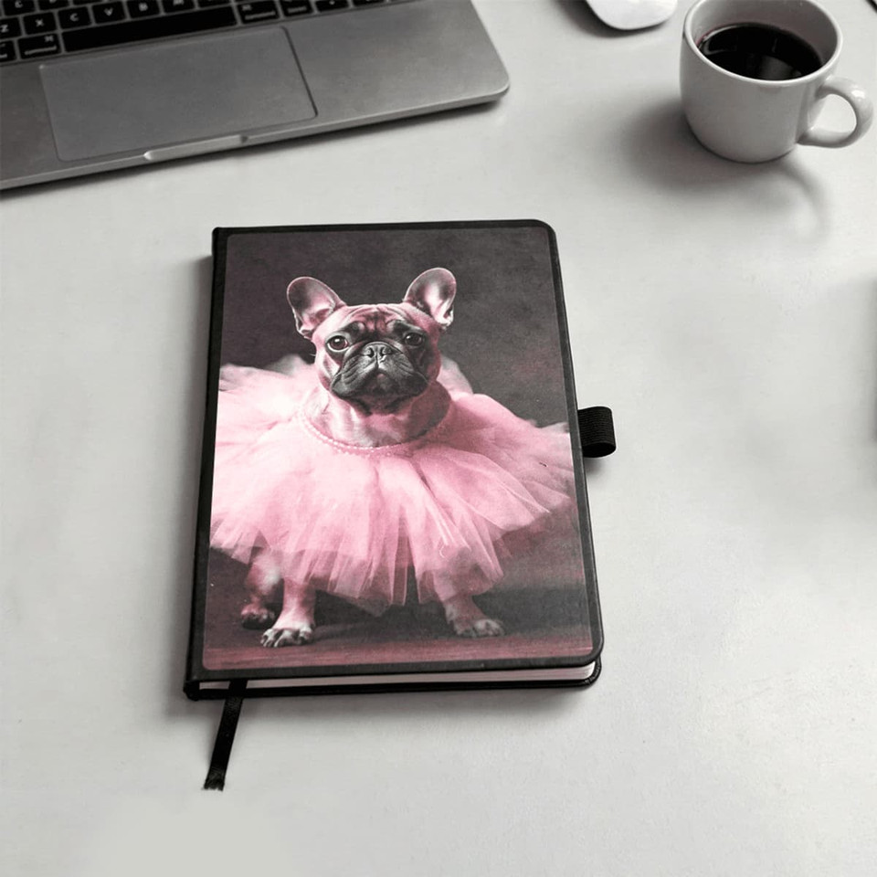 A notebook with a black cover featuring a pink tutu-wearing dog on the front. It includes a logo.
