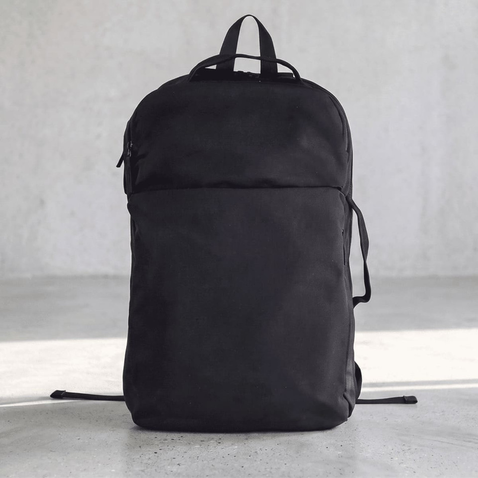A black backpack with a sleek design and a front pocket, featuring straps and a logo on the side.
