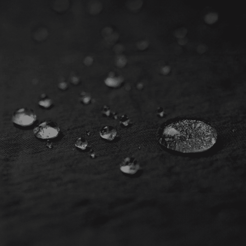 A close-up of water droplets on a textured black surface, showcasing various sizes and reflections.