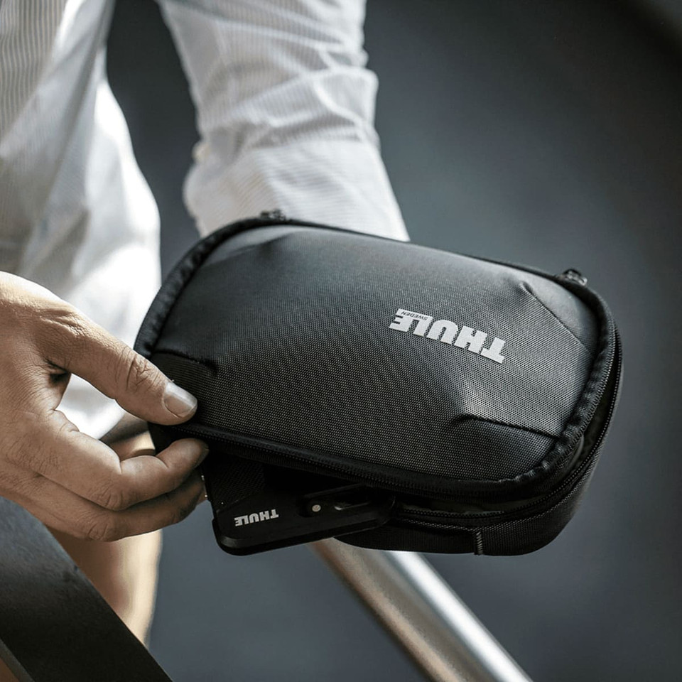 A black Thule Subterra PowerShuttle toiletry bag with a zipped compartment held in a person's hand.