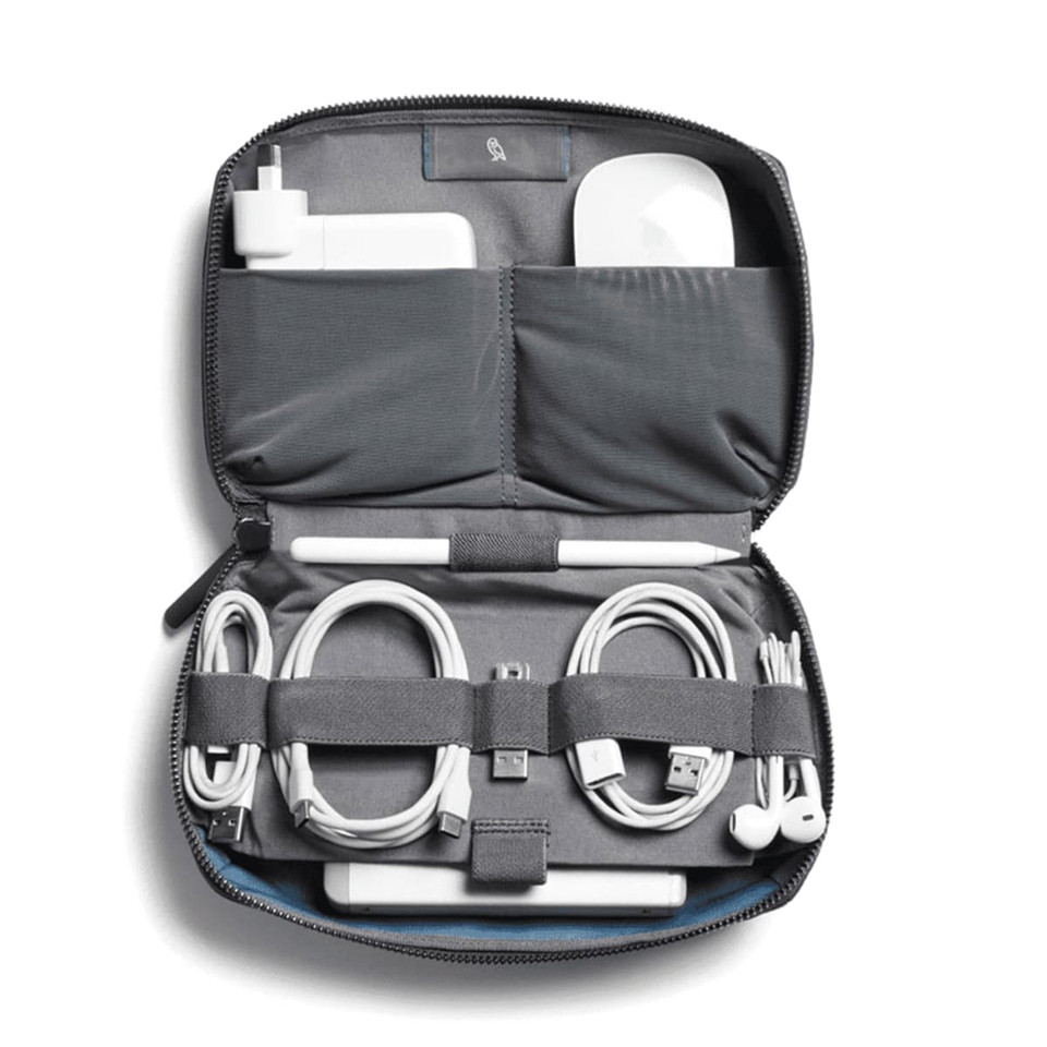 A grey tech kit featuring compartments for a charger, cables, and an airpod case, with a blue interior and a logo.