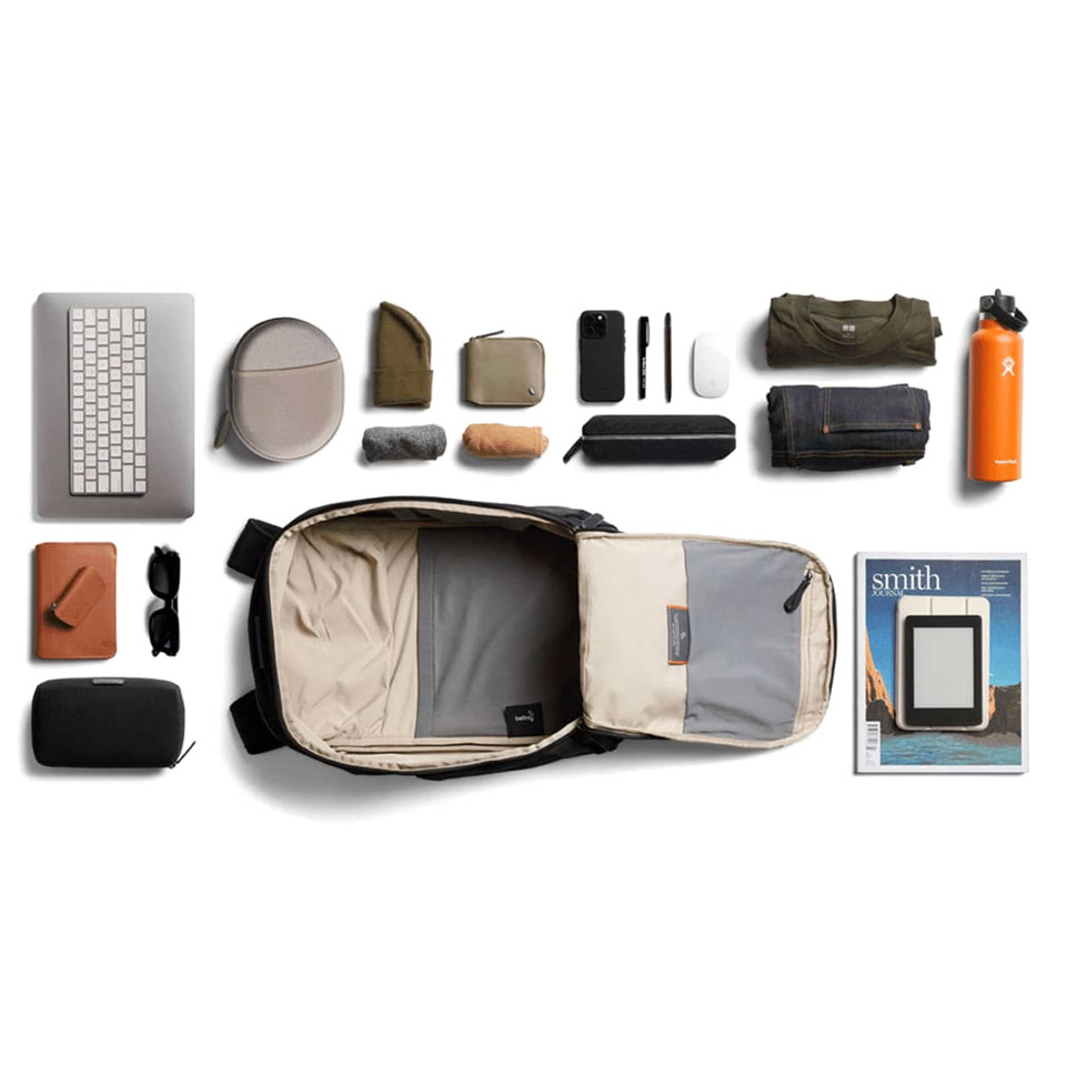 A black Bellroy Transit Workpack 20L with various contents including a laptop, pouches, clothing, and a drink bottle.