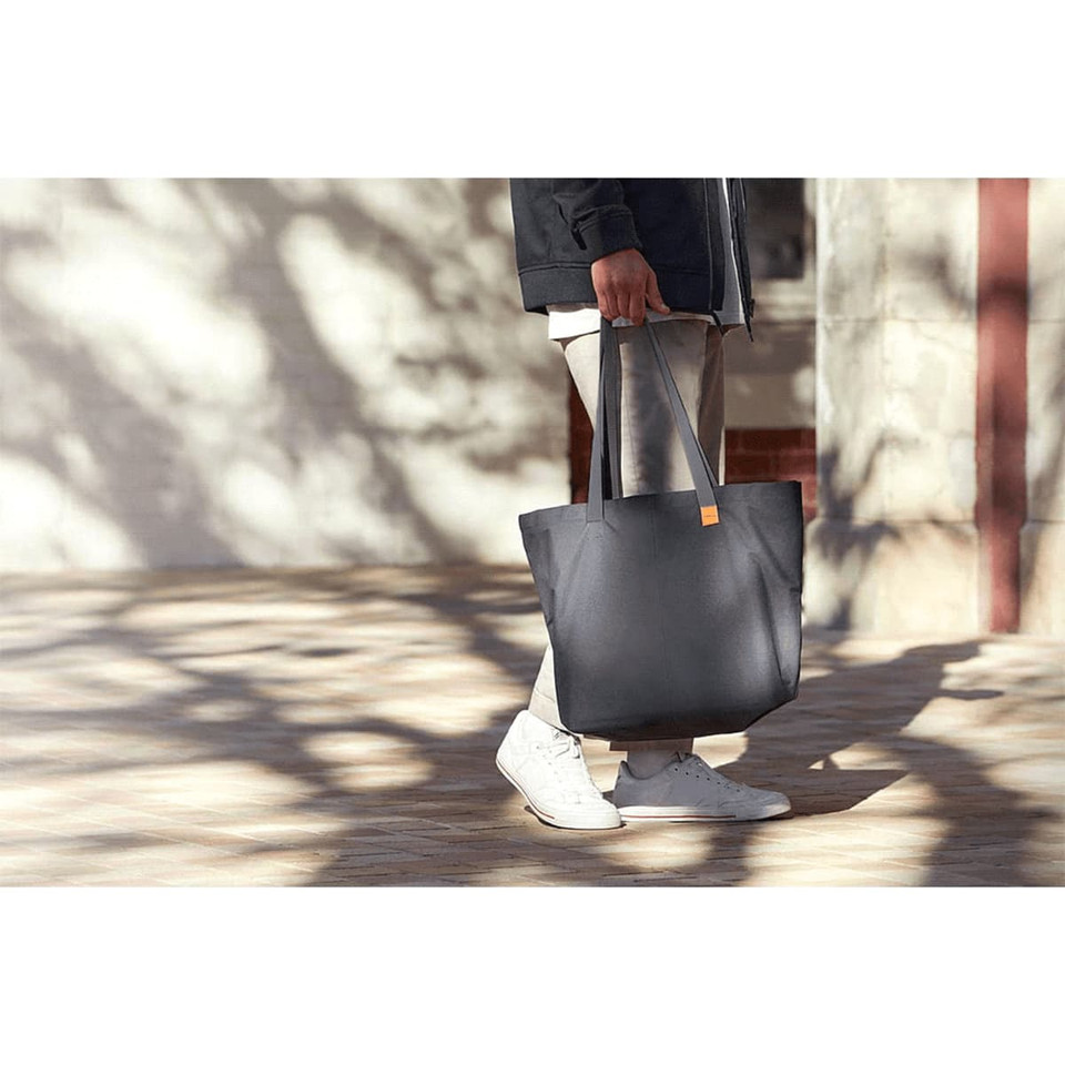 A person carries a large black tote bag with long handles, wearing light-coloured trousers and white shoes.