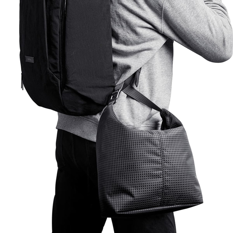 A cooler bag in a grid pattern, featuring a shoulder strap, being carried on the side of a person with a backpack.
