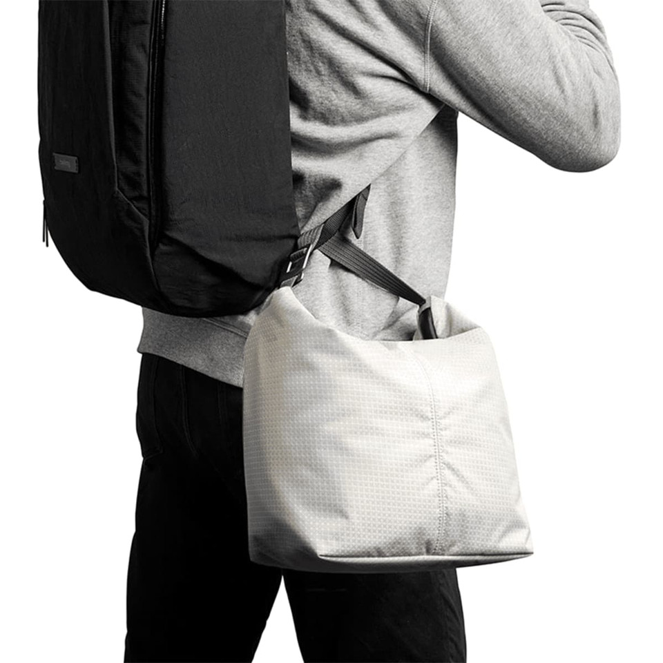 A light grey cooler bag is slung over the shoulder of a person wearing a black backpack and grey sweatshirt.
