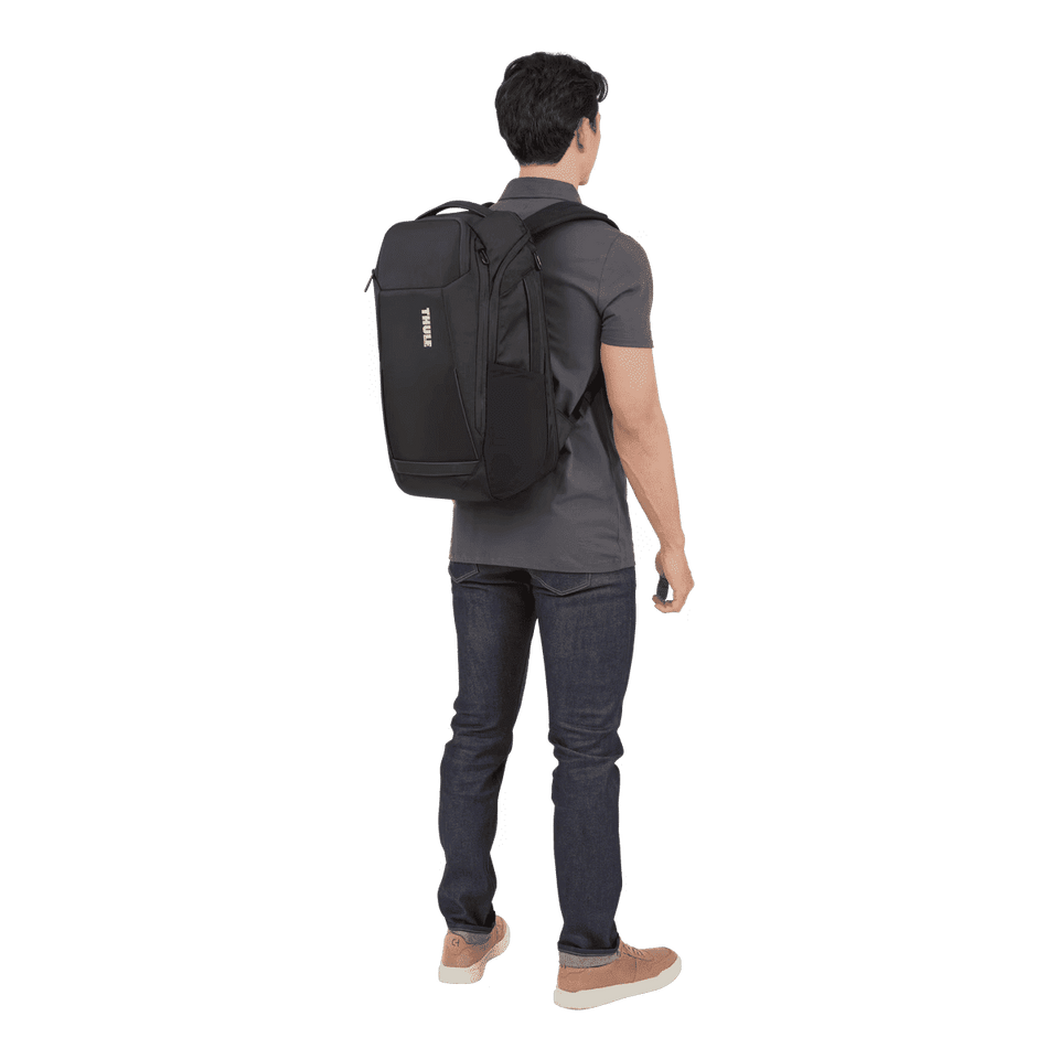 A black backpack worn on the back of a person dressed in a grey shirt and jeans. The backpack features a logo.