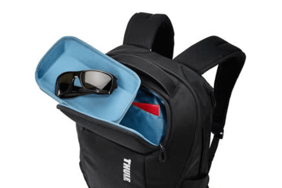 A black backpack with a blue-lined compartment, featuring sunglasses inside. It has adjustable shoulder straps and a logo.