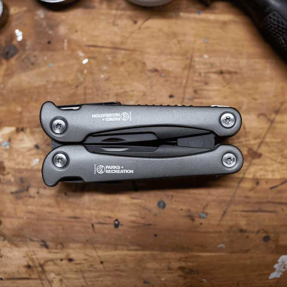 A grey multi-tool with multiple functions, featuring a sleek design and a logo, resting on a wooden surface.