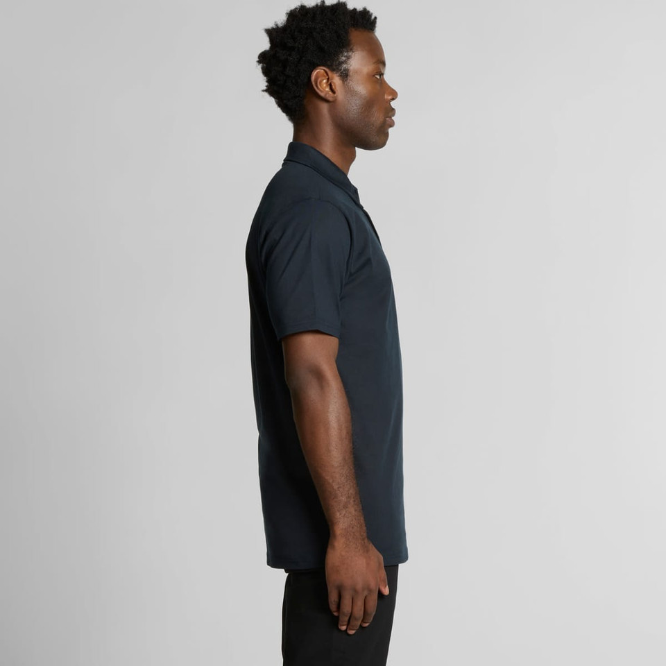 A black polo shirt is displayed on a model from the side, featuring a logo on the chest.