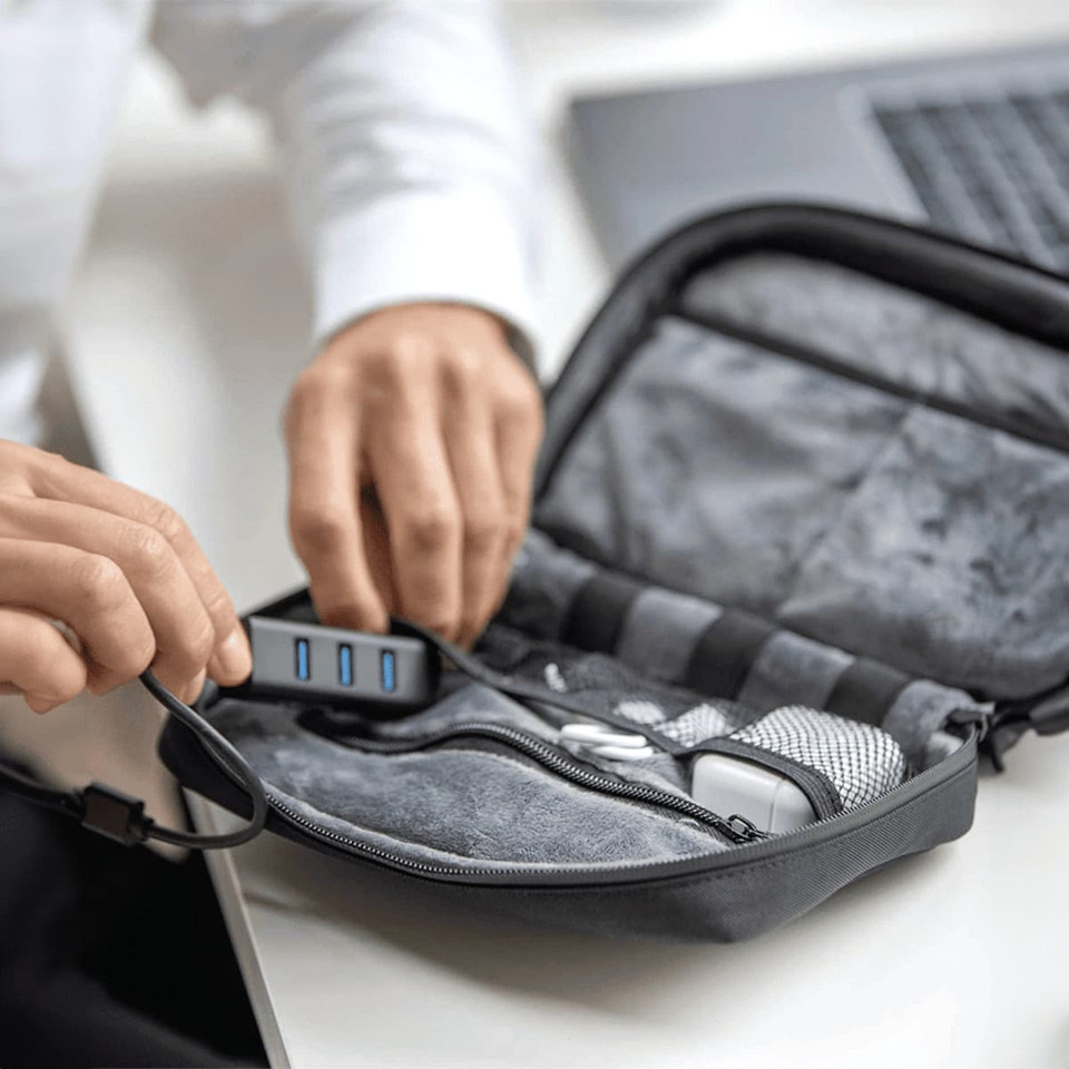 A grey organiser pouch with compartments, containing wires and electronics, being held open by a person.