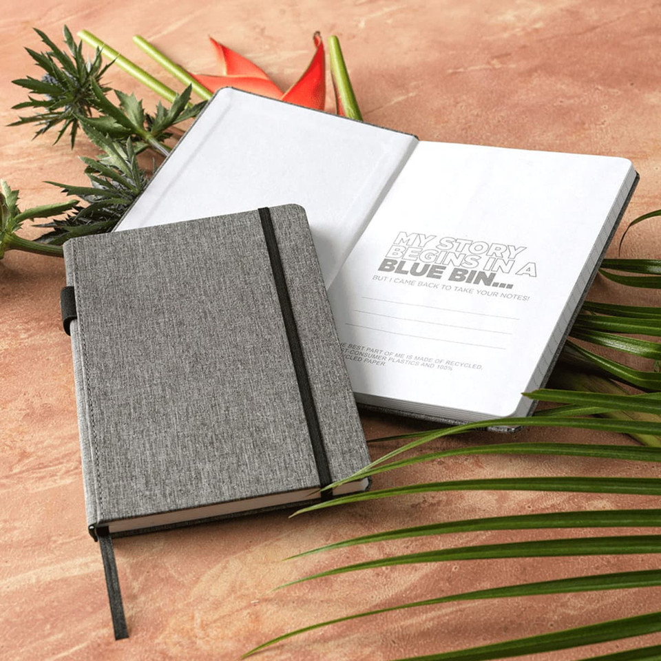 A grey A5 notebook with a textured cover, featuring an elastic band and blank inside pages. It has a logo.
