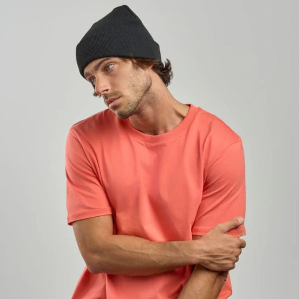 Man in a coral T-shirt and black beanie looking thoughtful.