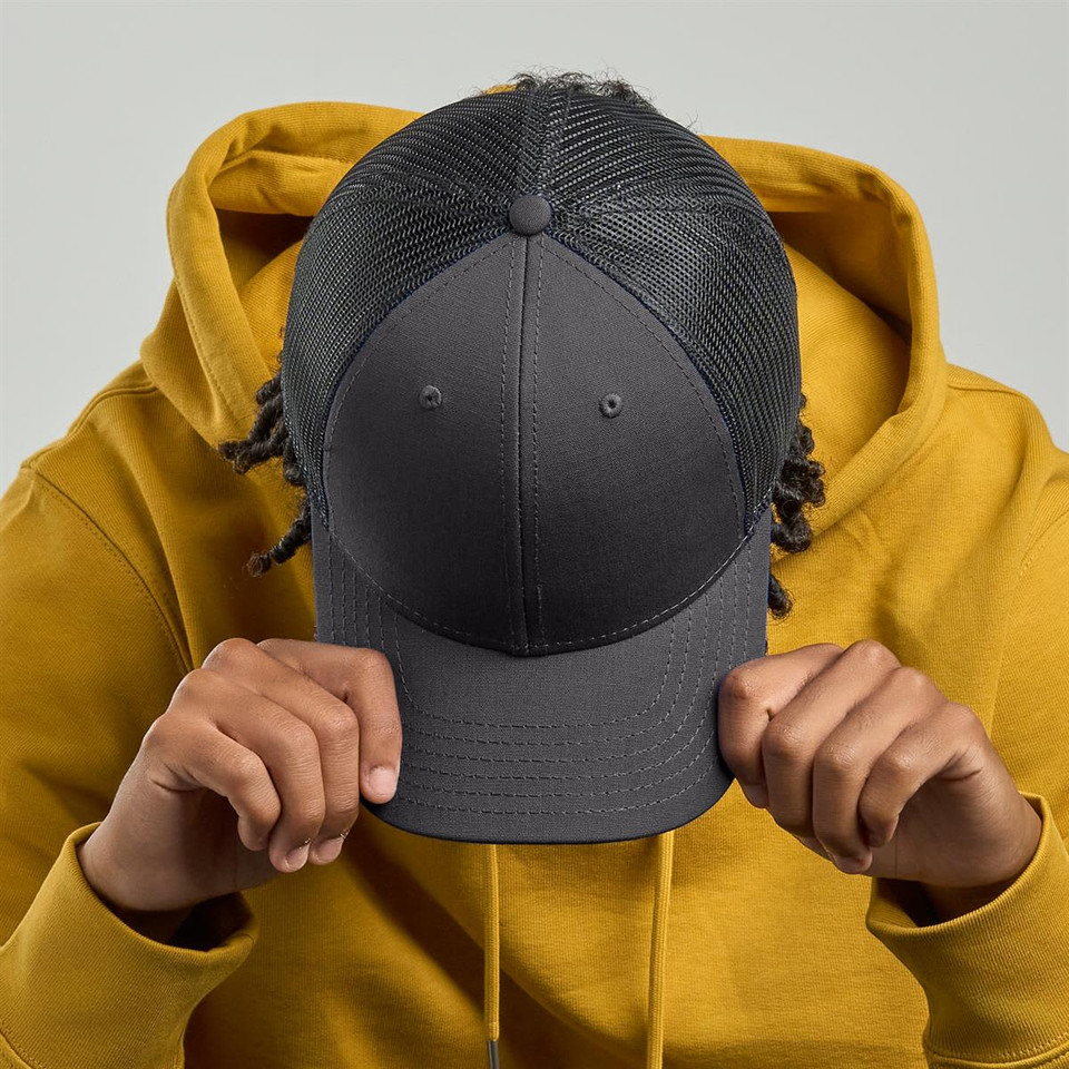 A grey cap with a mesh back is held by a person wearing a yellow hoodie, facing downwards.