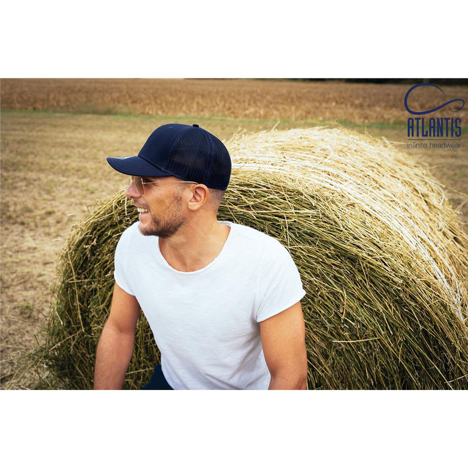 A navy cap resting on a man with short hair and glasses, sitting near a straw bale in a rural setting.