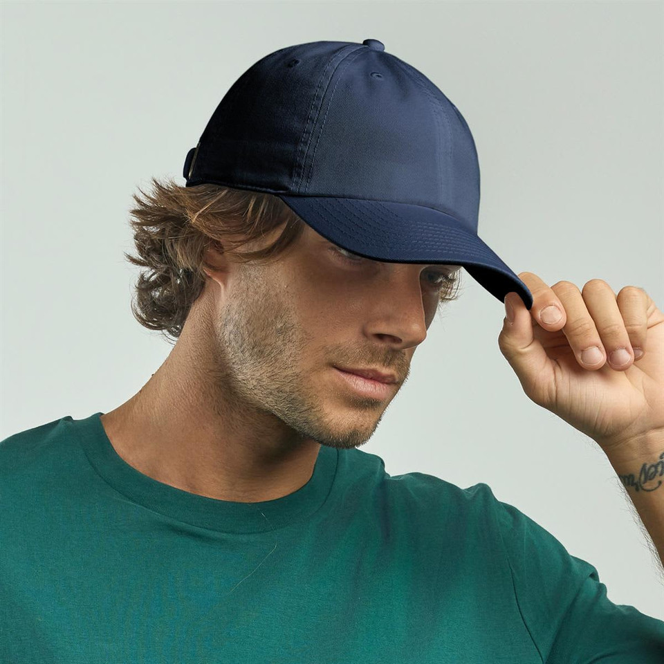 A navy organic dad hat is worn by a man with wavy hair, paired with a green shirt. The hat features a logo.