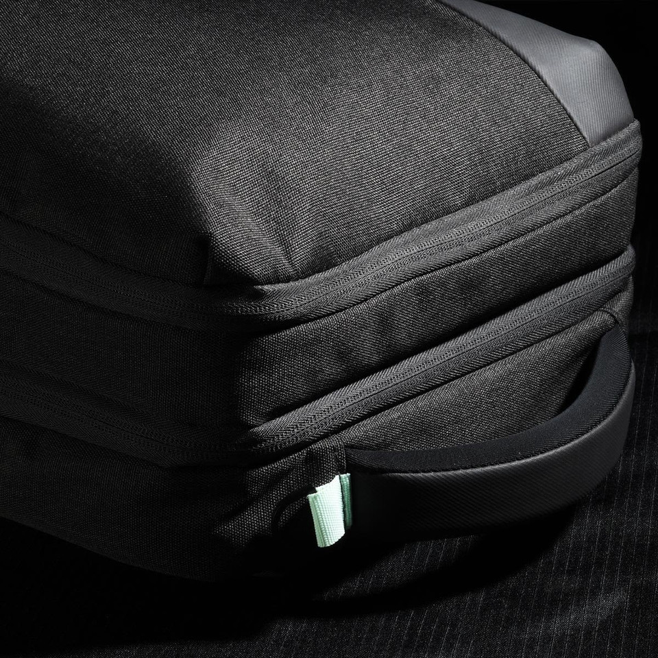 A black backpack with a textured exterior and a mint green zipper pull, featuring a side handle.