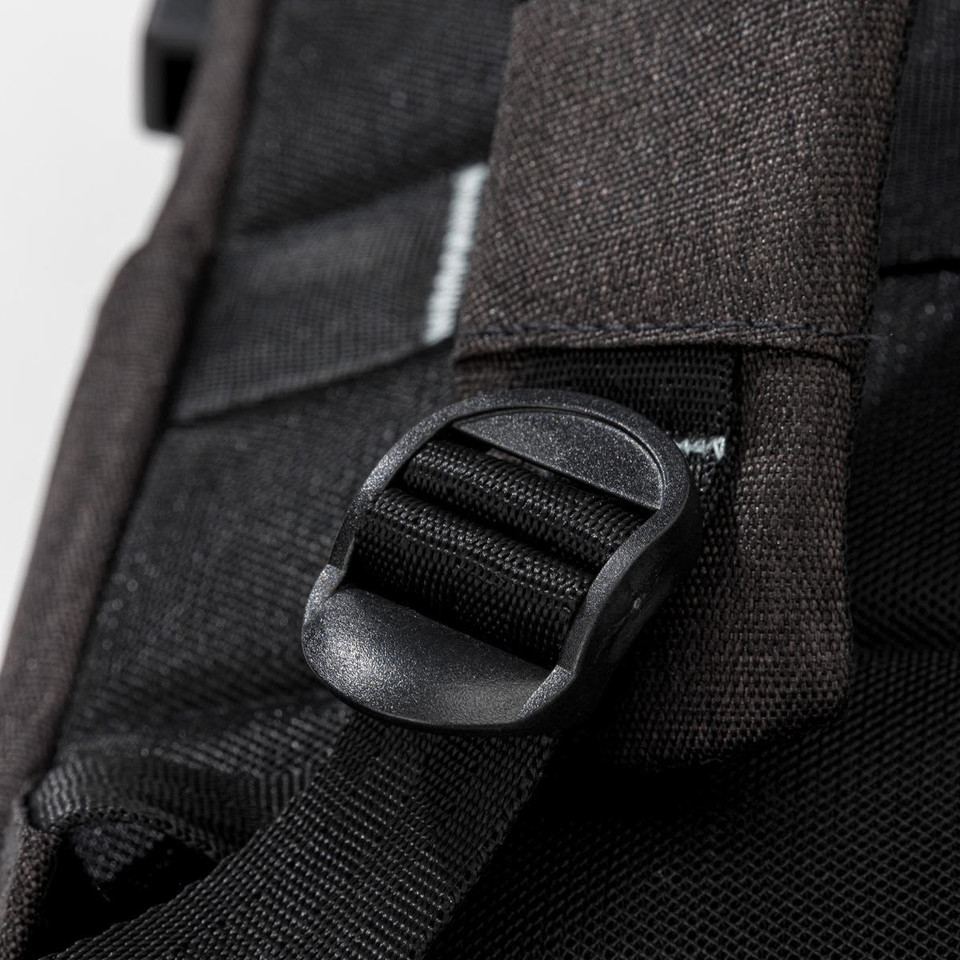 A close-up of a black backpack strap buckle with textured fabric in the background. The backpack has a logo.
