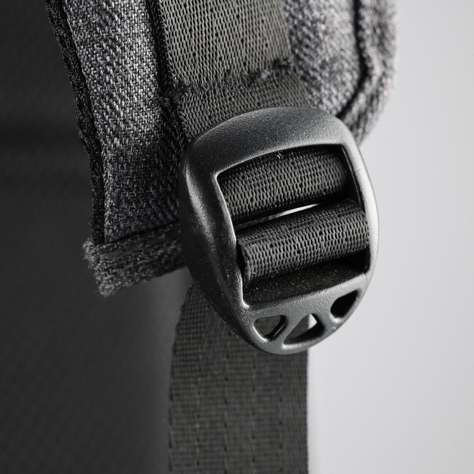 A close-up of a black buckle and strap on a grey backpack, featuring fabric detailing and stitching.