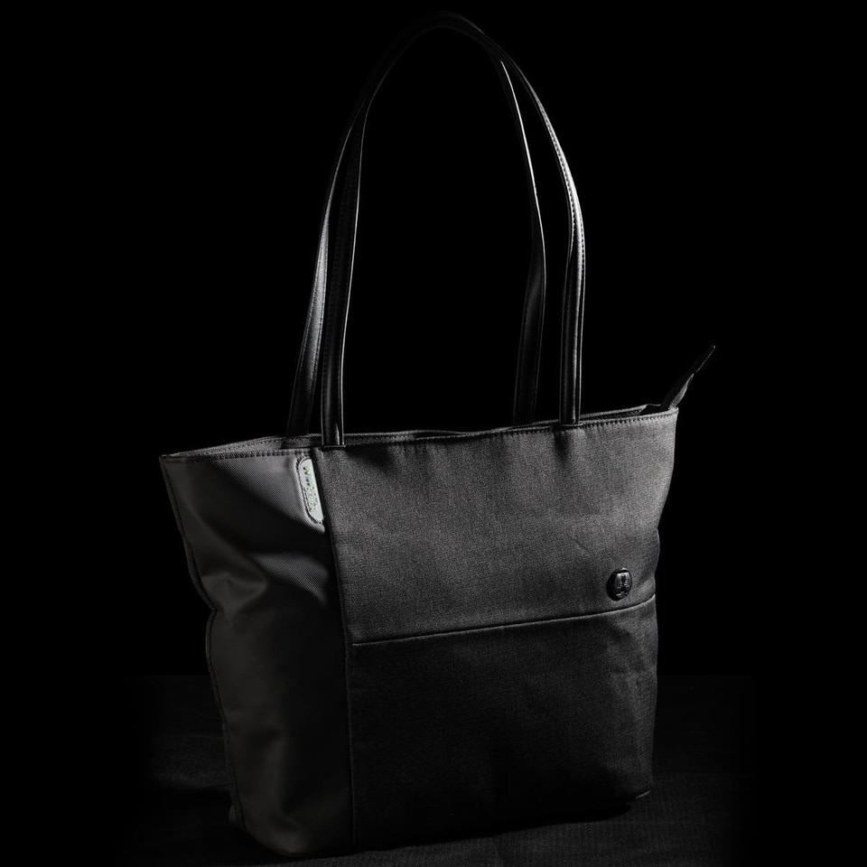 A black tote bag with leather handles and a front pocket, featuring a logo on the side.
