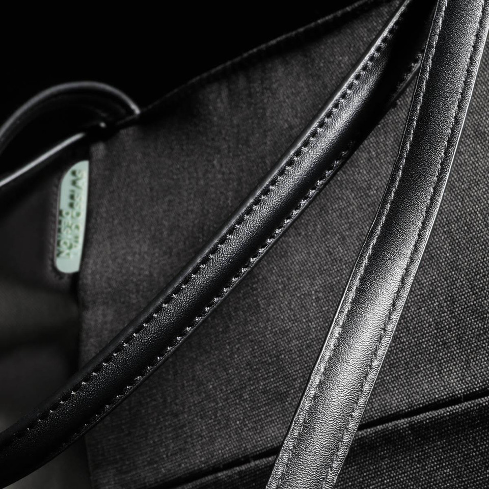 A black tote bag featuring a smooth, sleek handle and a subtle logo. The fabric has a textured finish.