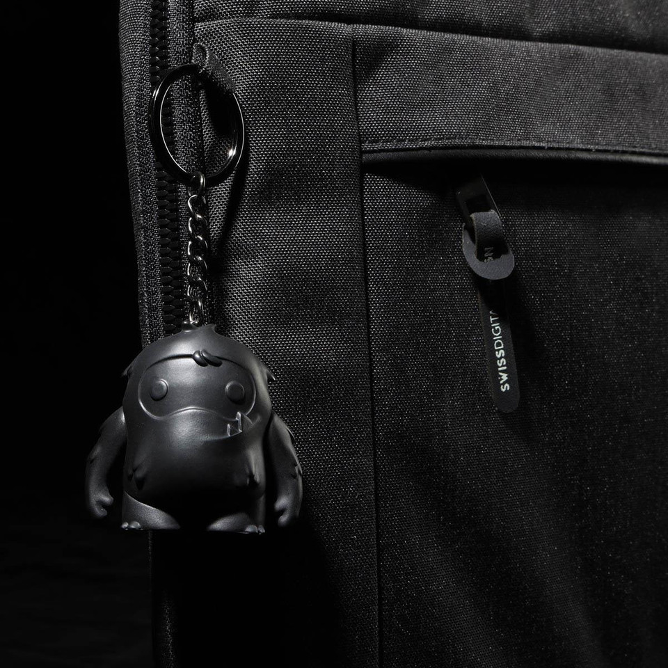 A black laptop sleeve features a textured surface and a keychain with a small black character.