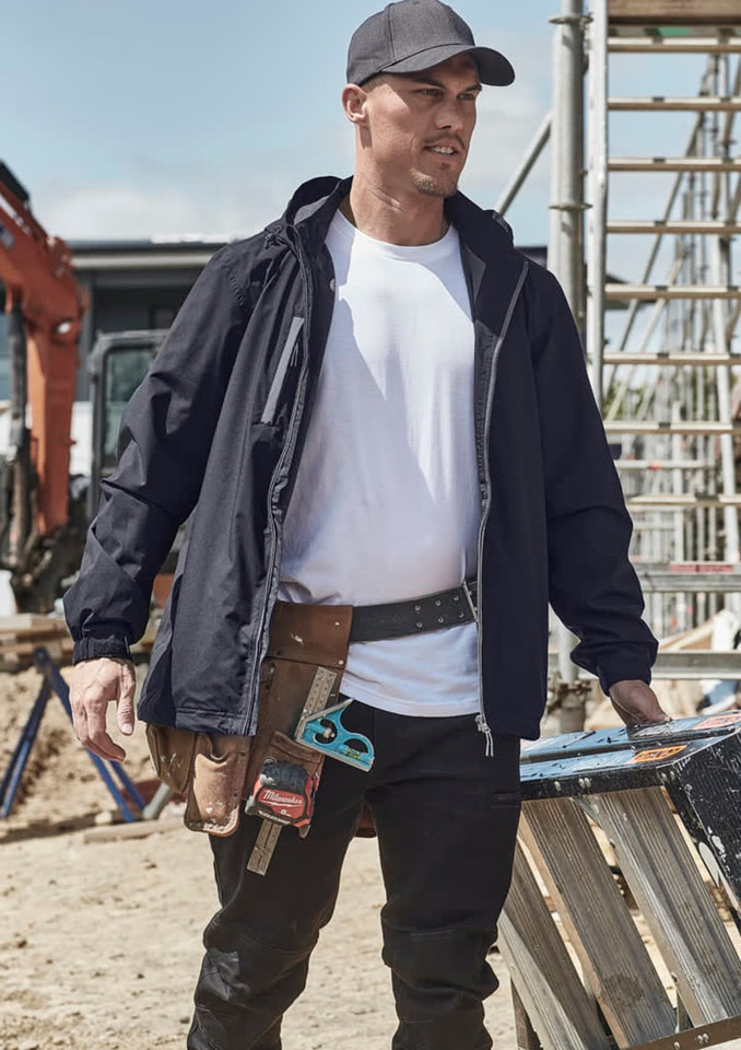 A man wearing a black unisex lightweight packable rain jacket, standing at a construction site with tools and equipment around.