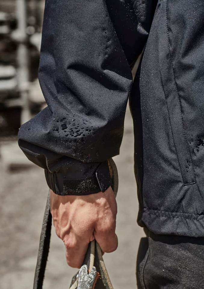 A close-up of a person's arm wearing a black packable rain jacket, holding a rope. The jacket features an adjustable cuff.