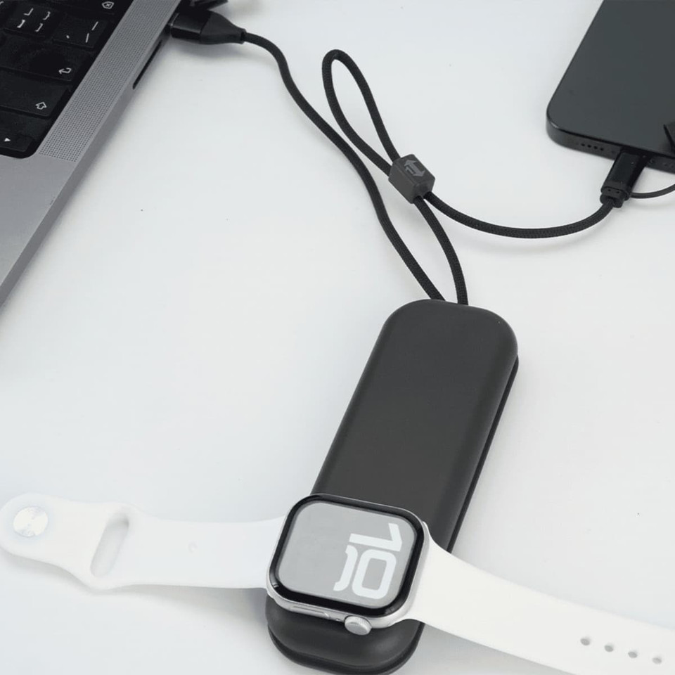 A black foldable charging cable with a wireless watch charger, connected to a laptop and a phone, next to a white watch.