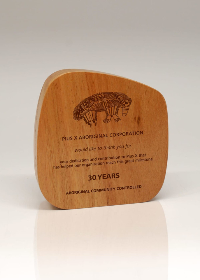 A wooden trophy with a curved shape, featuring an engraved design and text celebrating 30 years of achievement.