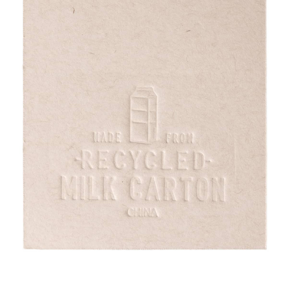 A beige bookmark shaped like a milk carton, made from recycled materials, featuring an embossed design and a logo.