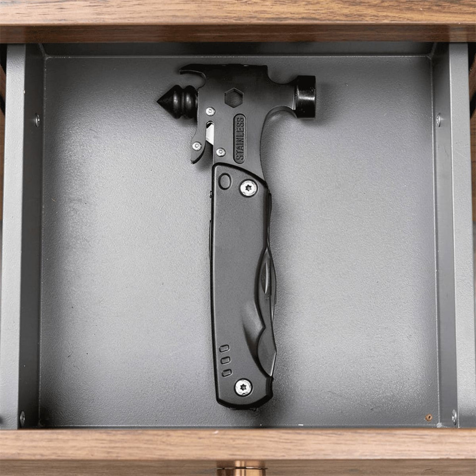 A black survival hammer with multiple tools, displayed in a grey drawer. It features a sleek design and a branding logo.