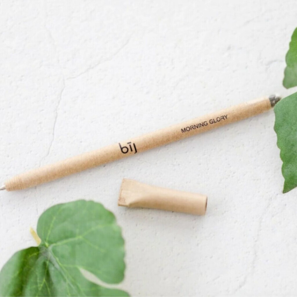 Eco-friendly pen with cap on white surface alongside green leaves.