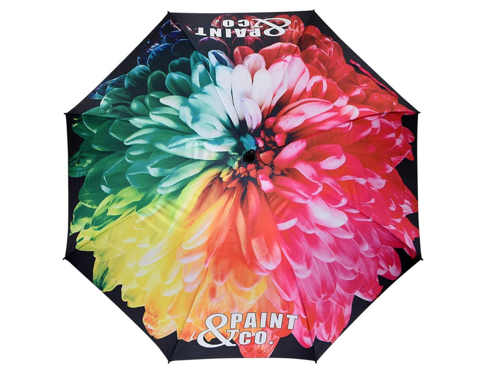 A large umbrella featuring a vibrant floral design in a mix of pink, green, and blue colours, with a logo on it.