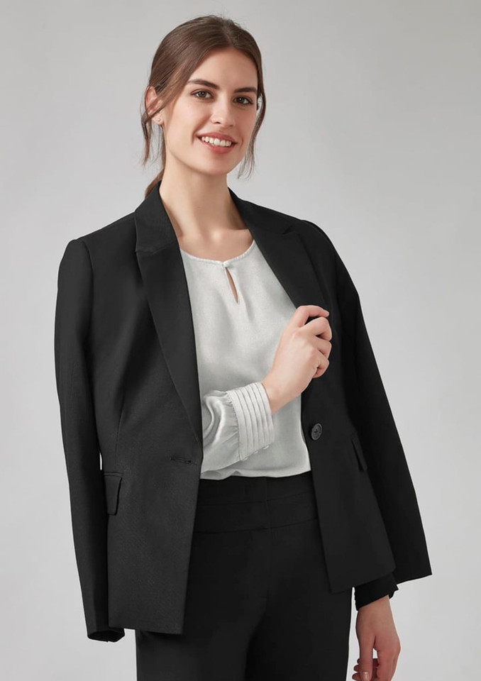 A woman wearing a black blazer over a white blouse, smiling at the camera. The outfit is polished and professional.