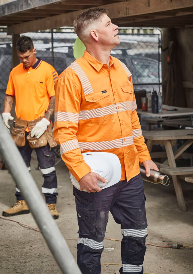 A bright orange men's work shirt with segmented tape, paired with navy pants, worn by a worker on site.