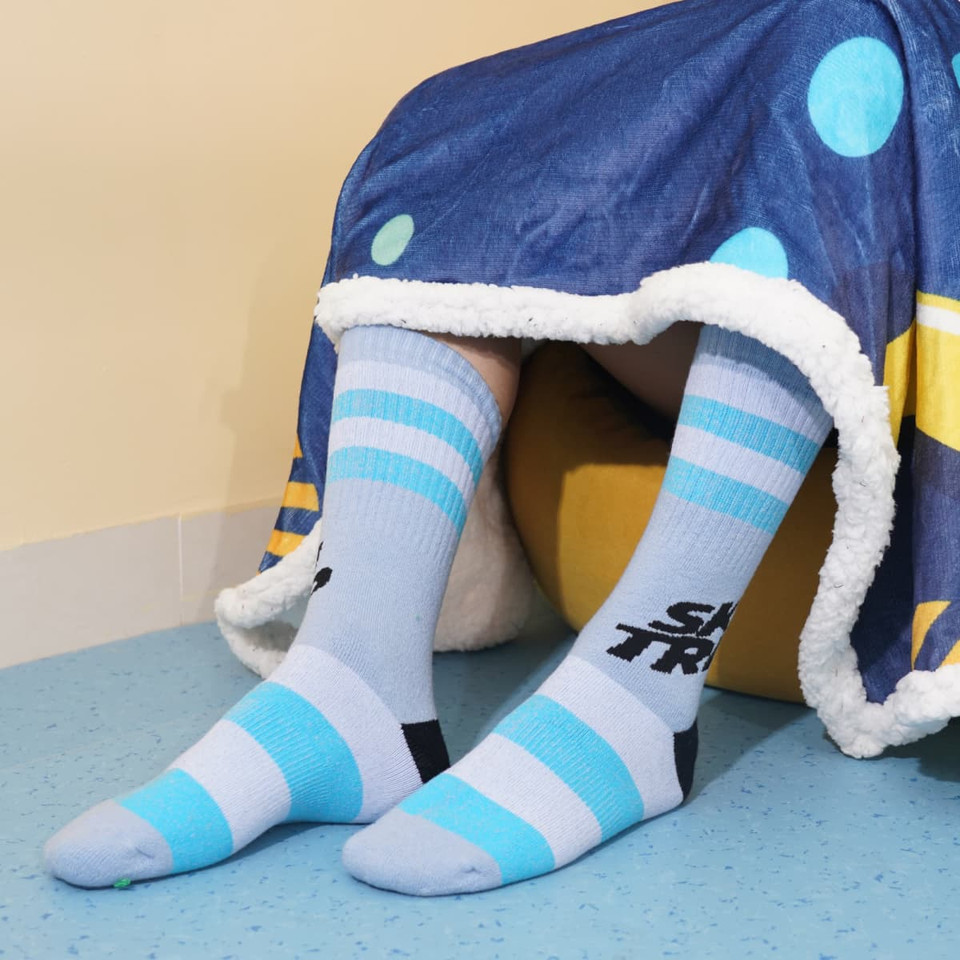 Light blue Merino wool socks with black and blue stripes, worn with a blanket draped over the legs.