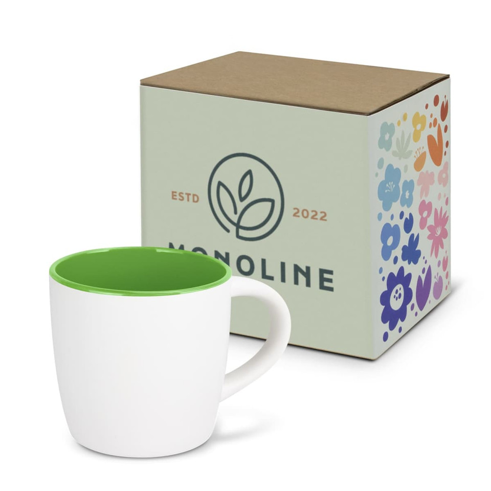 A two-tone coffee mug with a white exterior and green interior, next to a patterned cardboard box featuring a logo.