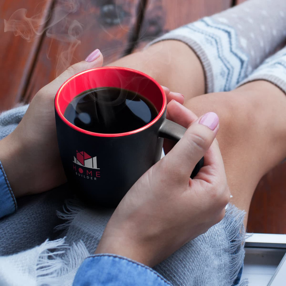 A two-tone mocha coffee mug with a black exterior and red interior, held by a person with grey socks.