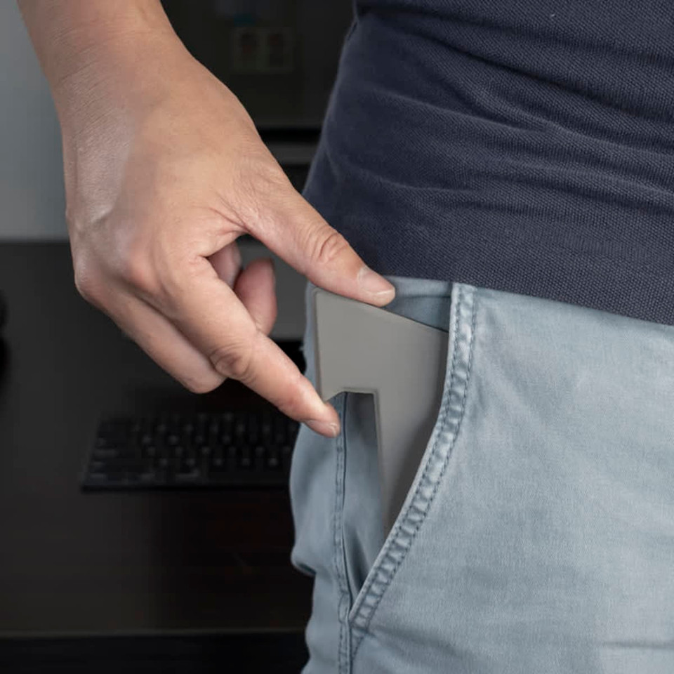 A grey phone stand is being inserted into a pocket, showcasing its compact design.